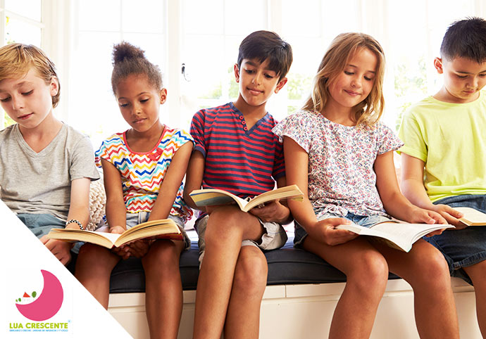 Grupo de crianças do 1.º Ciclo sentadas em fila enquanto leem livros.